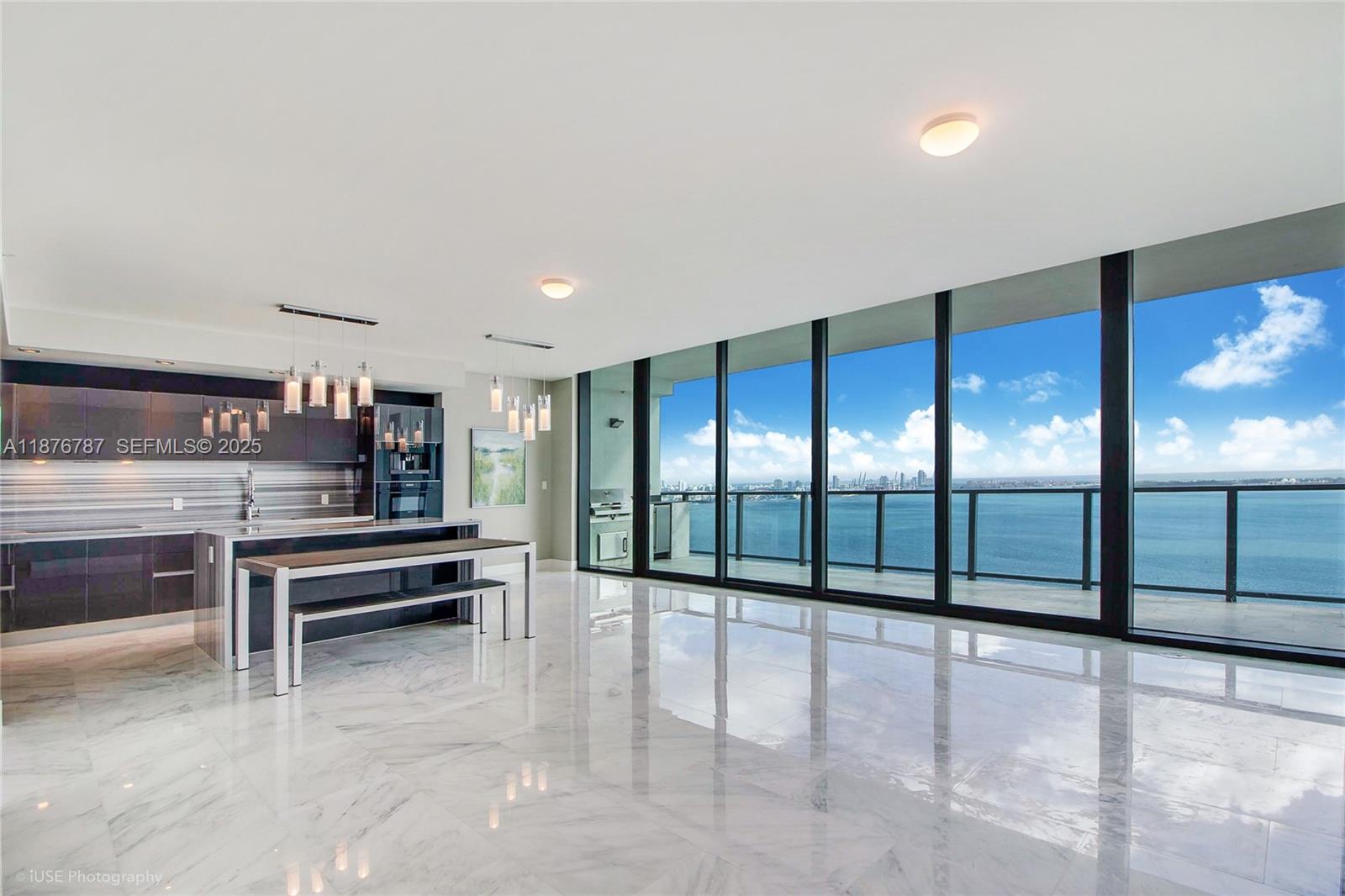 A modern kitchen with a dining island overlooks a balcony and the ocean through floor-to-ceiling windows — 1451 Brickell Ave # 3102, Miami FL 33131, MIAMI, FL