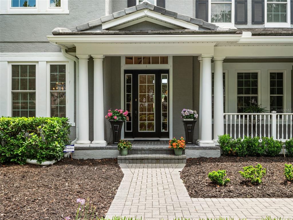 A gray house exterior features a covered porch with white columns and a brick walkway — 25622 HAWKS RUN LANE, SORRENTO, FL