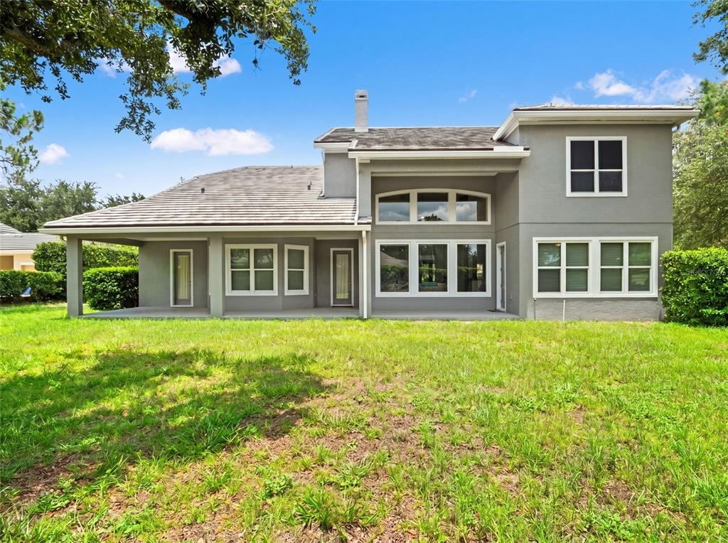 The rear exterior of a two-story gray house features a covered patio and large windows — 25622 HAWKS RUN LANE, SORRENTO, FL