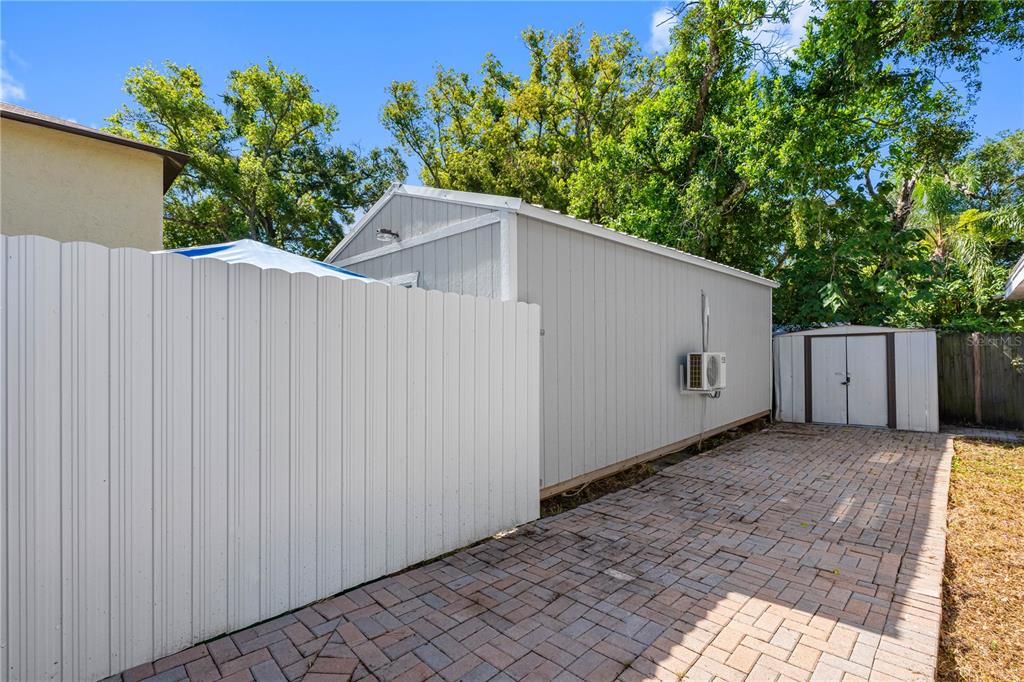 A gray shed with an air conditioning unit sits on a paved patio behind a fence — 1205 E SENECA AVENUE, TAMPA, FL