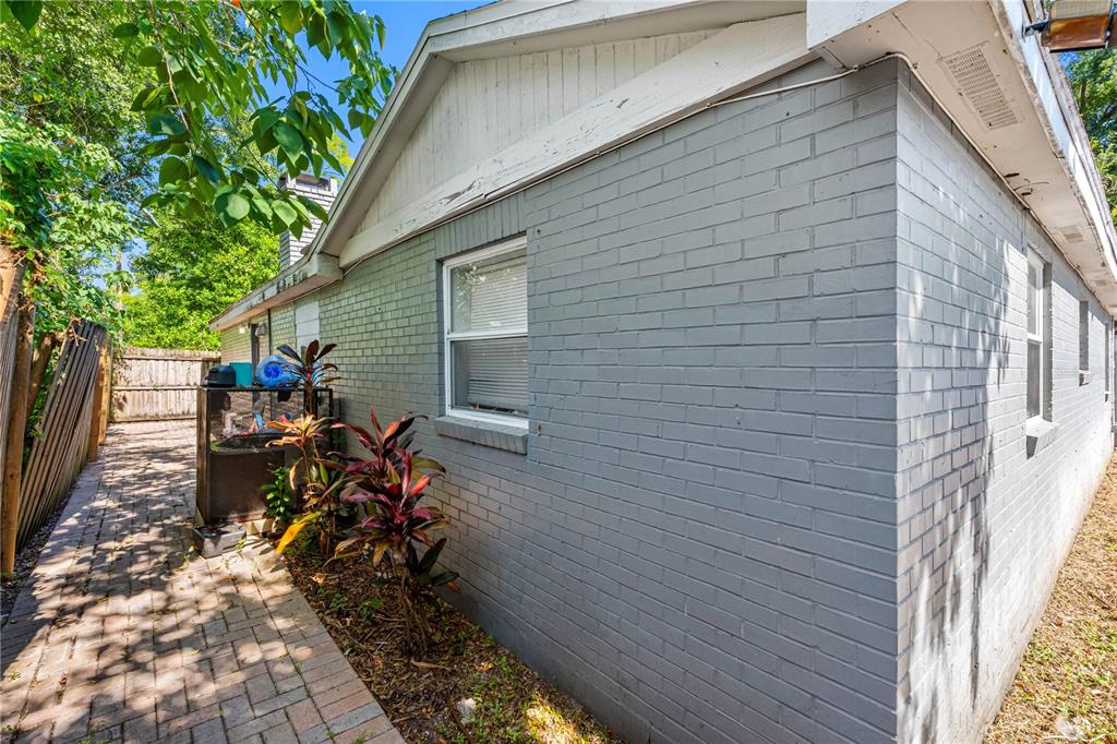 A side view of a gray brick house exterior with a paved walkway and landscaping — 1205 E SENECA AVENUE, TAMPA, FL
