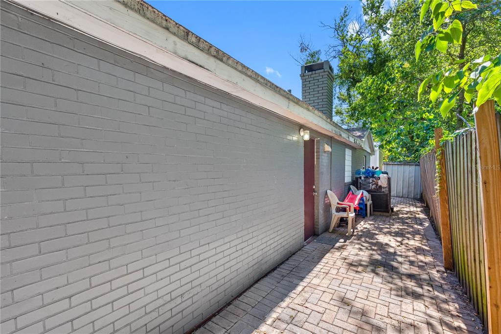 A paved side yard features a gray brick wall, a red door, and a chimney — 1205 E SENECA AVENUE, TAMPA, FL