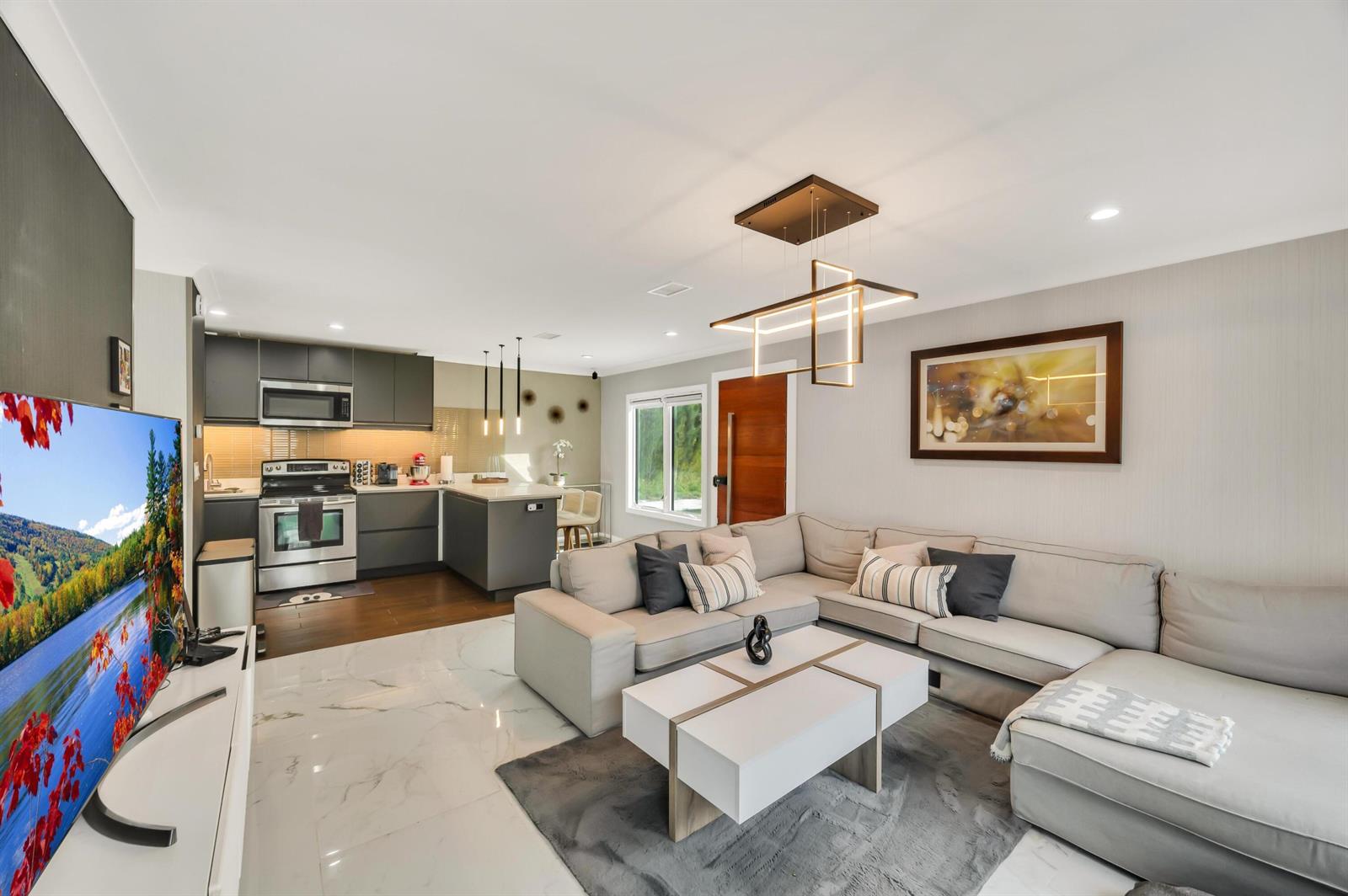 An open-concept living room and kitchen featuring a sectional sofa, marble flooring, and modern lighting — 6320 86th Lane, Vero Beach FL 32967, VERO BEACH, FL