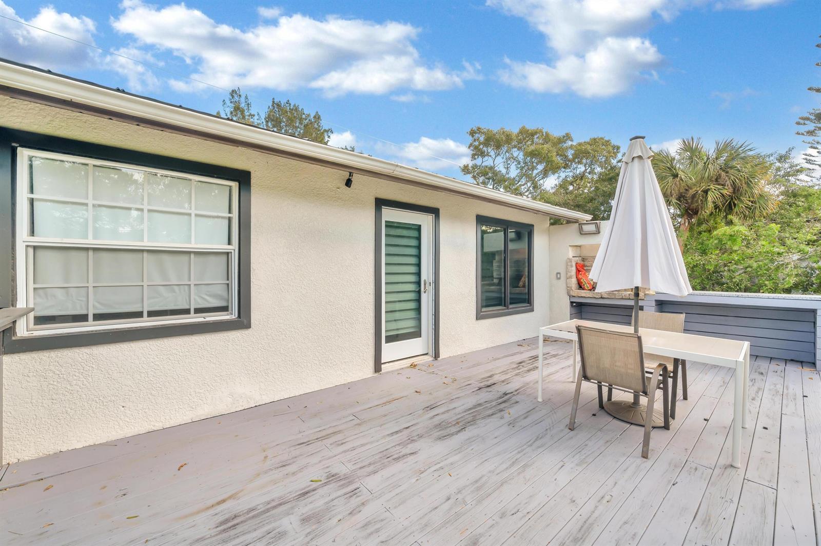 A wooden deck features a dining set with an umbrella outside a stucco house — 6320 86th Lane, Vero Beach FL 32967, VERO BEACH, FL
