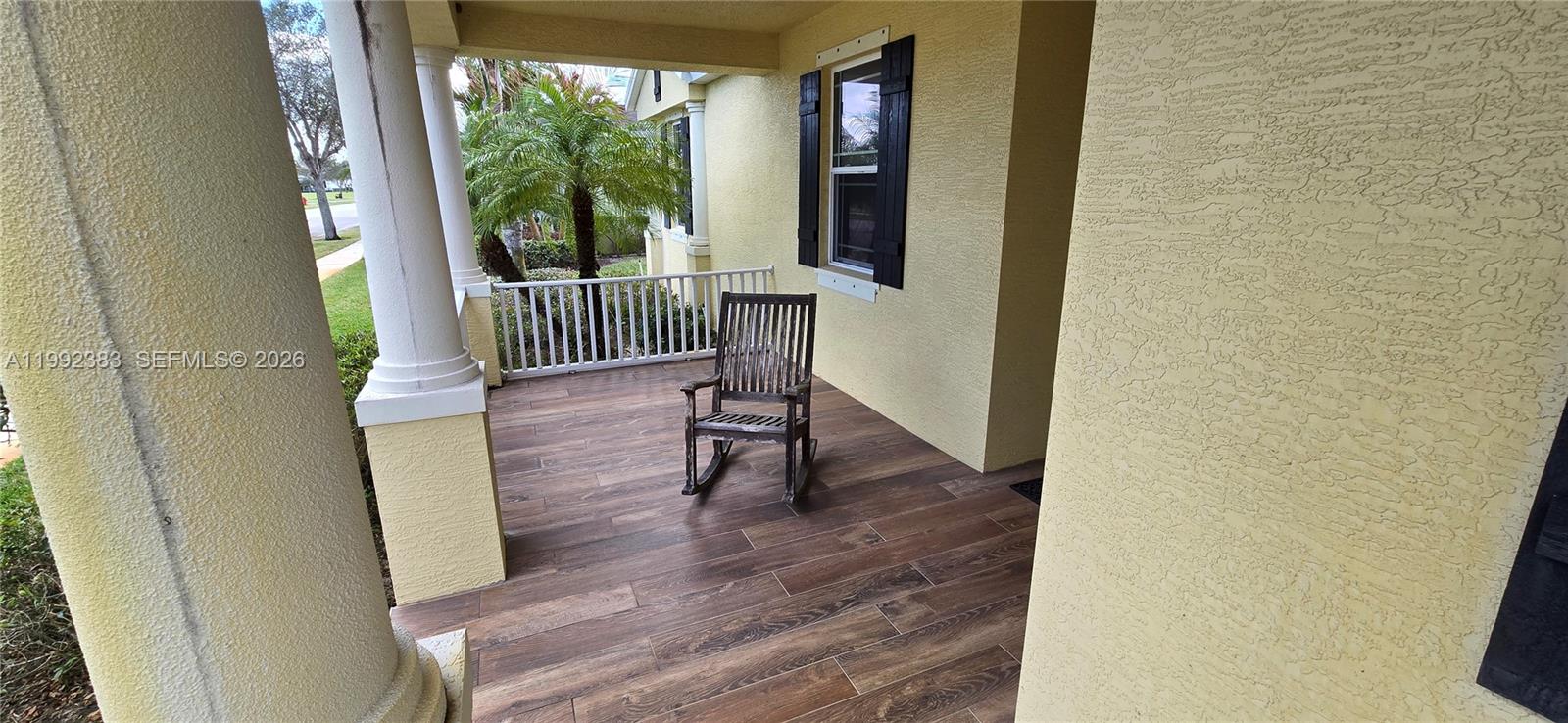 A covered porch features wood-look tile flooring, a white railing, and a wooden rocking chair — 1460 Caddy Ct, Vero Beach FL 32966, VERO BEACH, FL