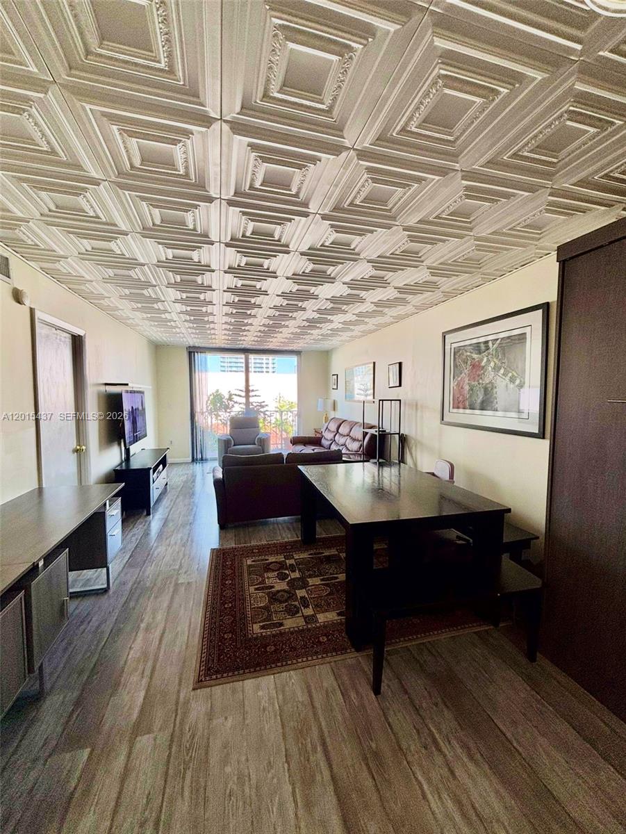 A living and dining area features a coffered ceiling, wood-look flooring, and a balcony view — 6801 Indian Creek Dr # 402, Miami Beach FL 33141, MIAMI BEACH, FL