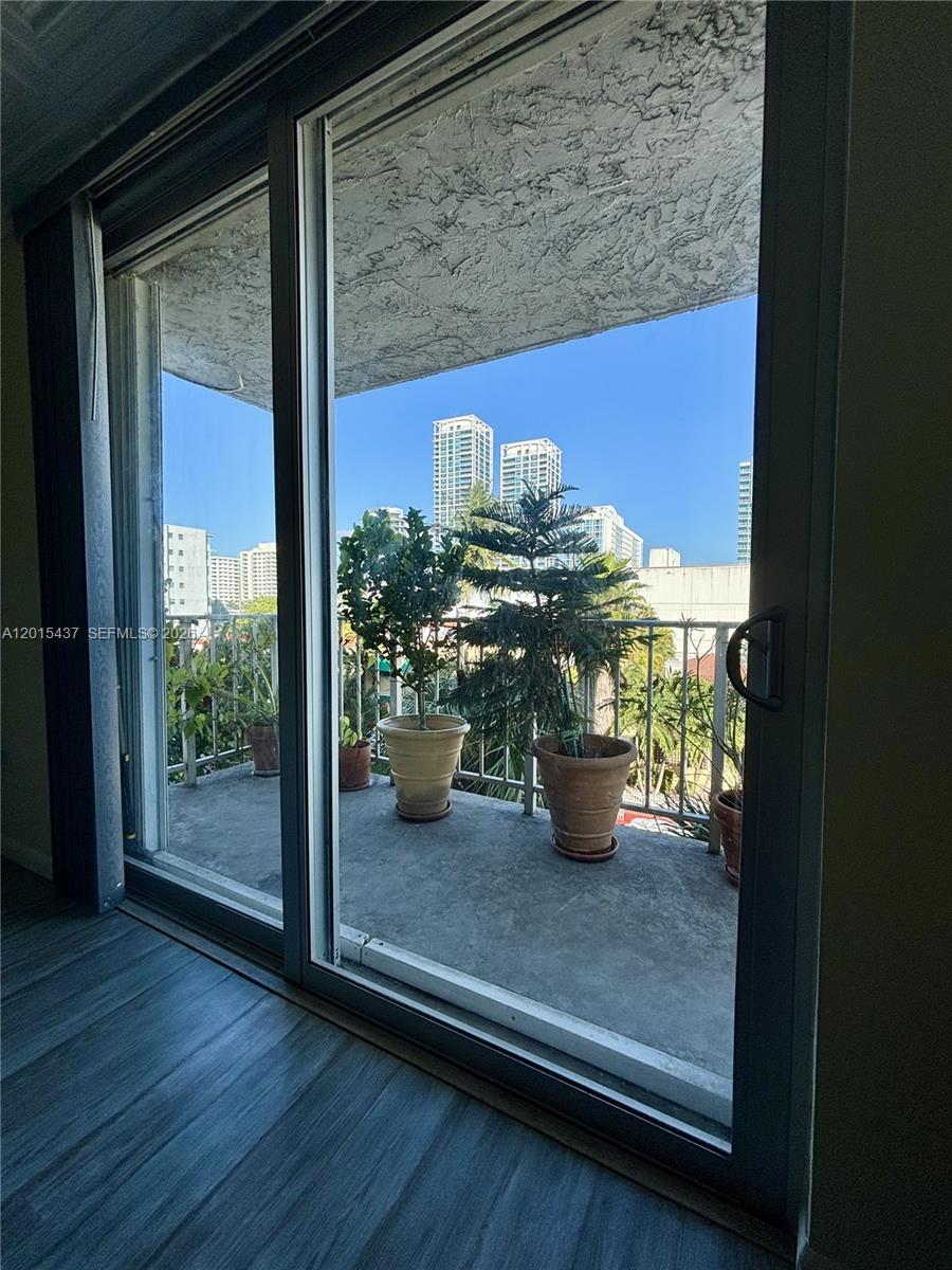 A balcony with potted plants overlooks a city skyline through a sliding glass door — 6801 Indian Creek Dr # 402, Miami Beach FL 33141, MIAMI BEACH, FL