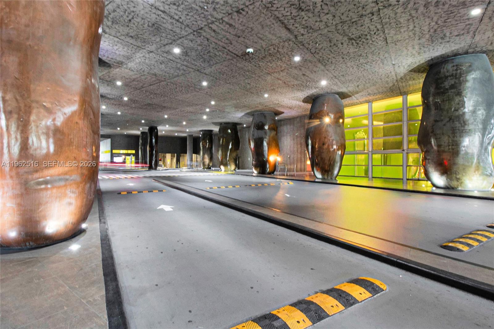 A modern parking garage features large, sculptural columns and yellow-striped speed bumps on the pavement — 465 Brickell Ave # 5102, Miami FL 33131, MIAMI, FL