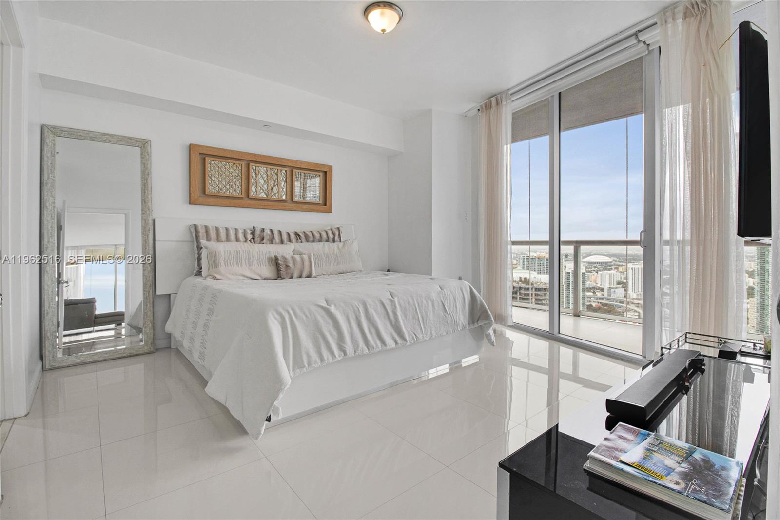 A modern bedroom features a white bed, a floor mirror, and a balcony with city views — 465 Brickell Ave # 5102, Miami FL 33131, MIAMI, FL