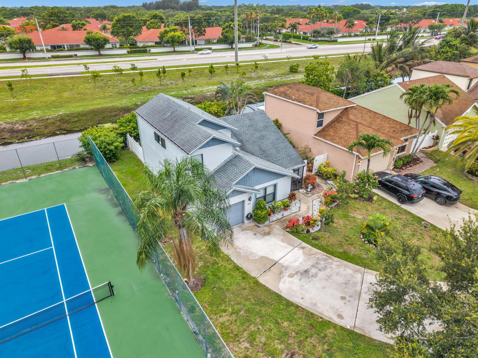 An aerial view shows a house with a gray roof next to a tennis court — 143 W Tara Lakes Dr Drive W, Boynton Beach FL 33436, BOYNTON BEACH, FL