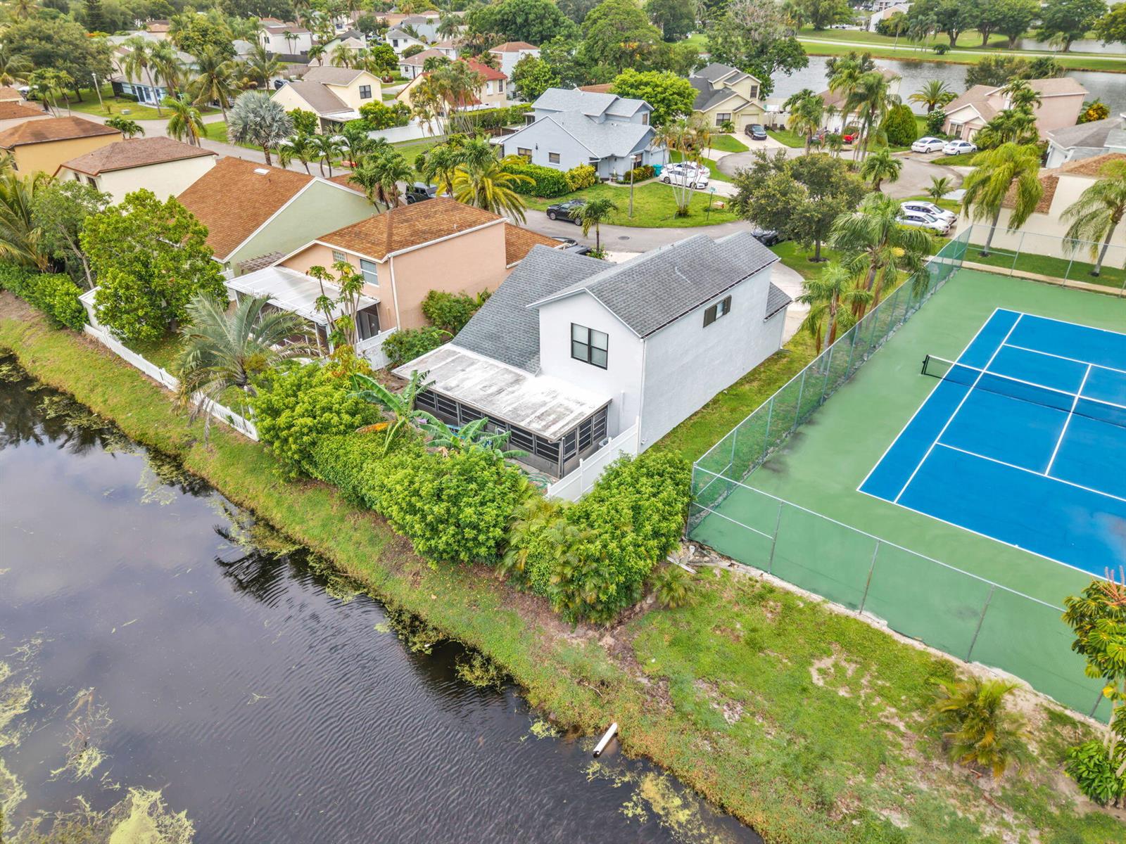 An aerial view shows a house with a screened patio next to a tennis court — 143 W Tara Lakes Dr Drive W, Boynton Beach FL 33436, BOYNTON BEACH, FL