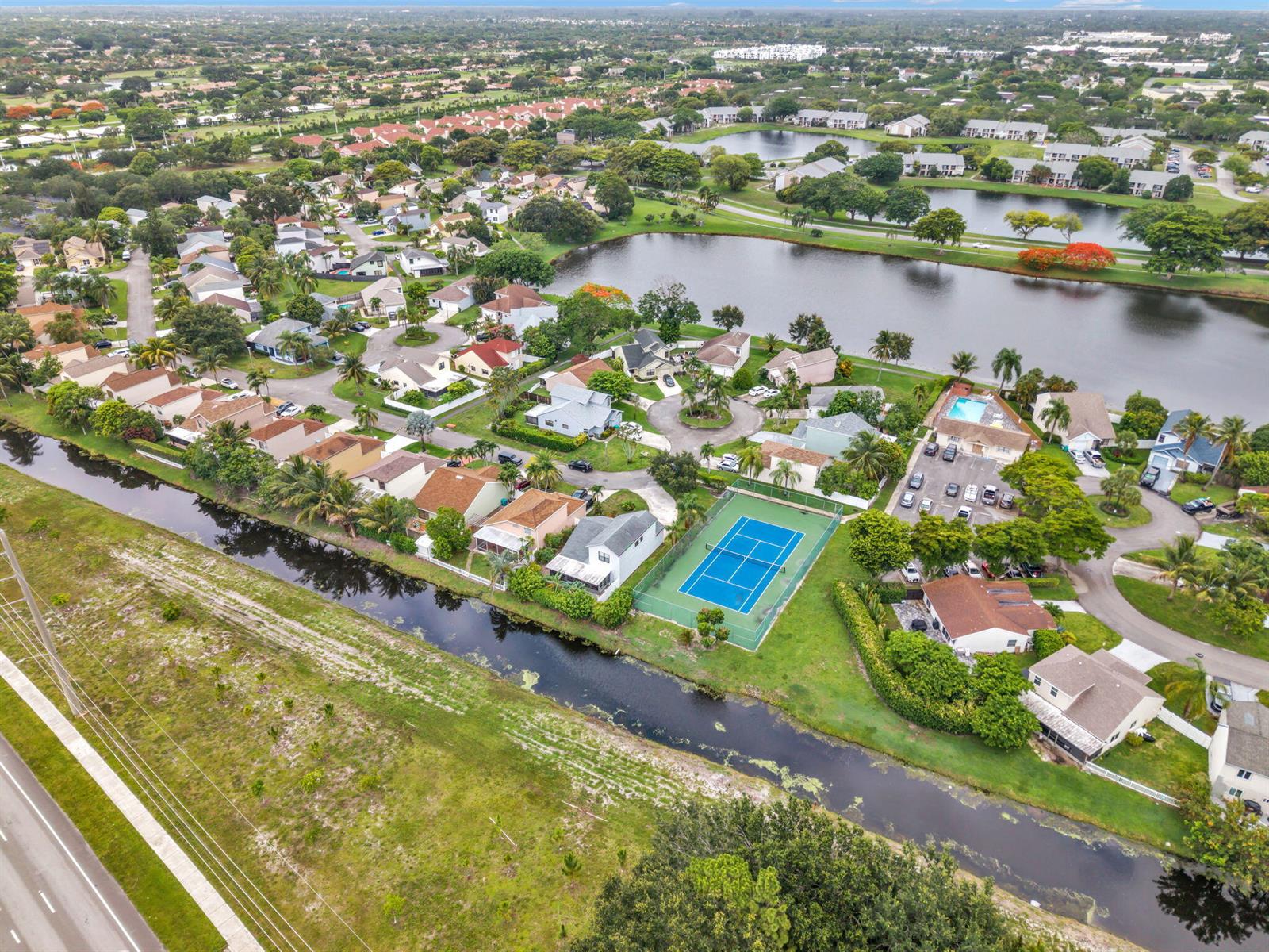 An aerial view shows a residential neighborhood with a tennis court, canal, and lake — 143 W Tara Lakes Dr Drive W, Boynton Beach FL 33436, BOYNTON BEACH, FL