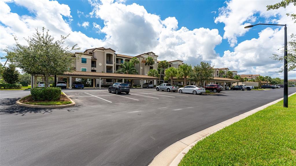 A multi-story apartment building with covered parking spaces in a paved lot under a cloudy sky — 17108 VARDON TERRACE UNIT 206, BRADENTON, FL