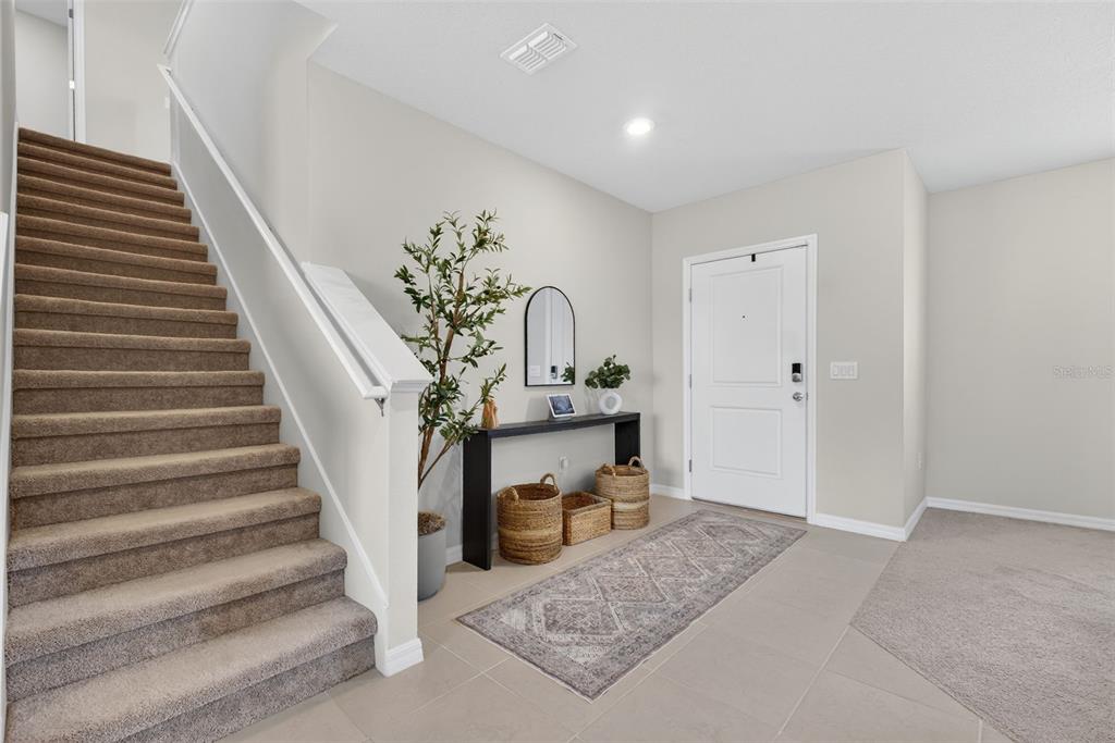 A carpeted staircase leads up from a tiled entryway featuring a console table and rug — 1117 MICHELANGELO LANE, WINTER HAVEN, FL