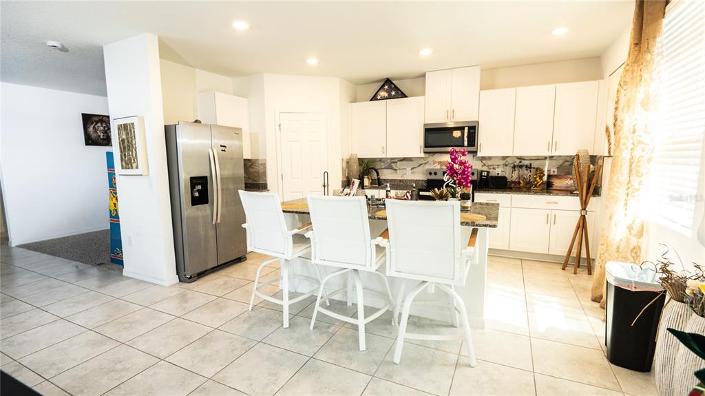 A kitchen features white cabinets, stainless steel appliances, a granite island, and three white chairs — 3198 VICEROY COURT, POINCIANA, FL