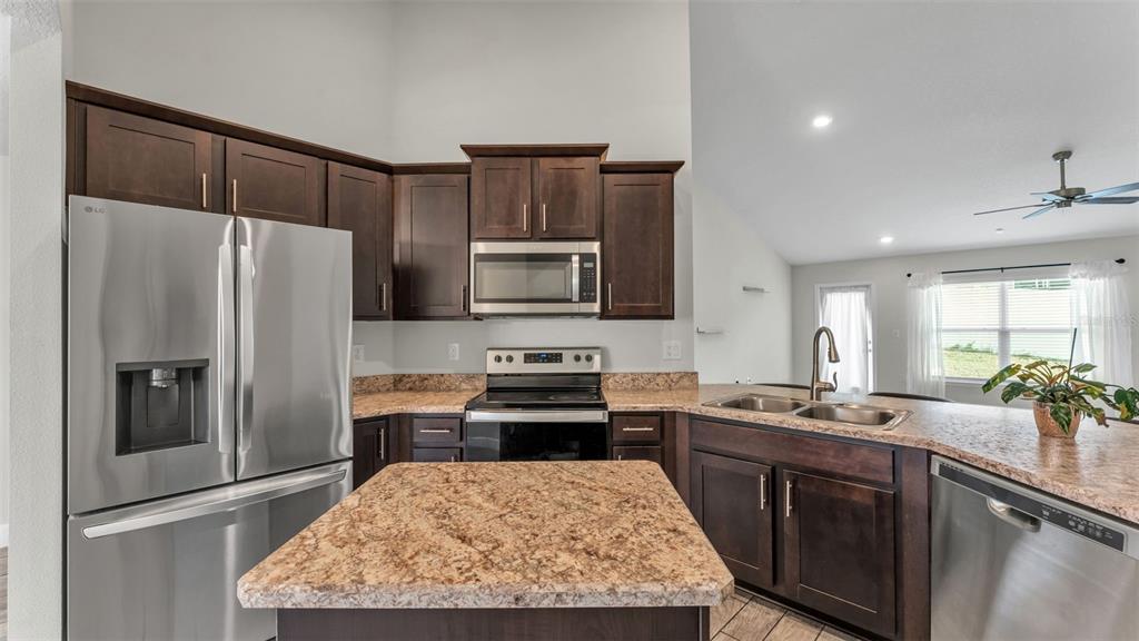 A kitchen features dark wood cabinets, granite countertops, stainless steel appliances, and a central island — 310 ATHABASCA PLACE, POINCIANA, FL
