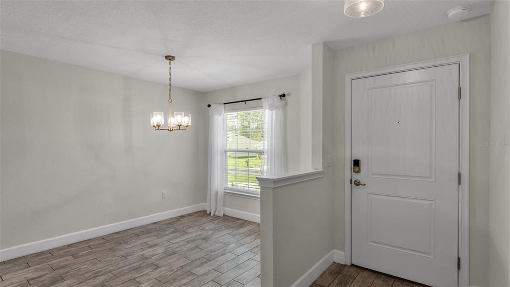 A dining area features wood-look tile flooring, a chandelier, and a white front door — 310 ATHABASCA PLACE, POINCIANA, FL
