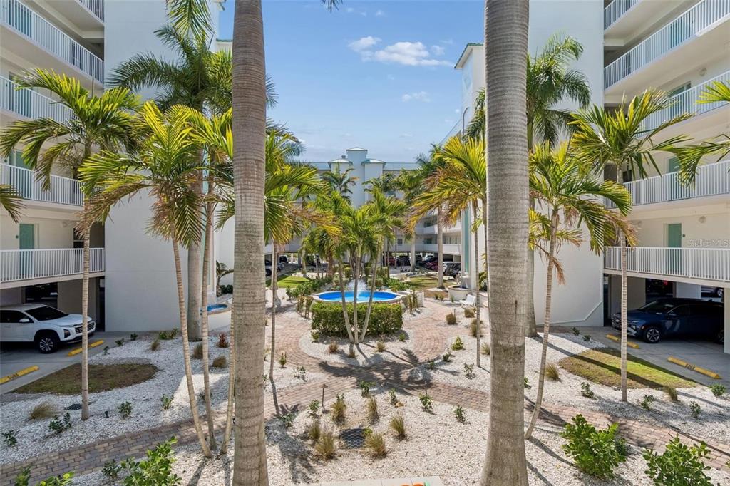 A courtyard with a central fountain, palm trees, and covered parking between two apartment buildings — 12000 GULF BOULEVARD UNIT 603N, TREASURE ISLAND, FL