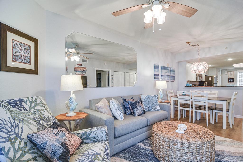 A living and dining area features a gray sofa, patterned armchair, and a wicker ottoman — 12000 GULF BOULEVARD UNIT 603N, TREASURE ISLAND, FL