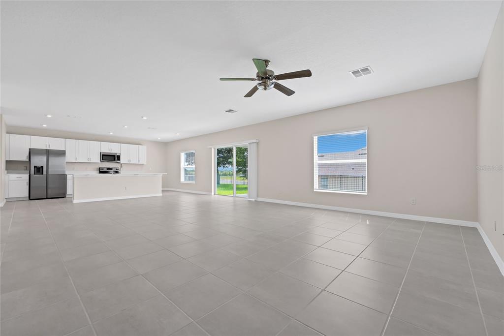 A spacious, open-concept living area with light tile flooring, a kitchen, and a ceiling fan — 3800 FESCUE STREET, CLERMONT, FL