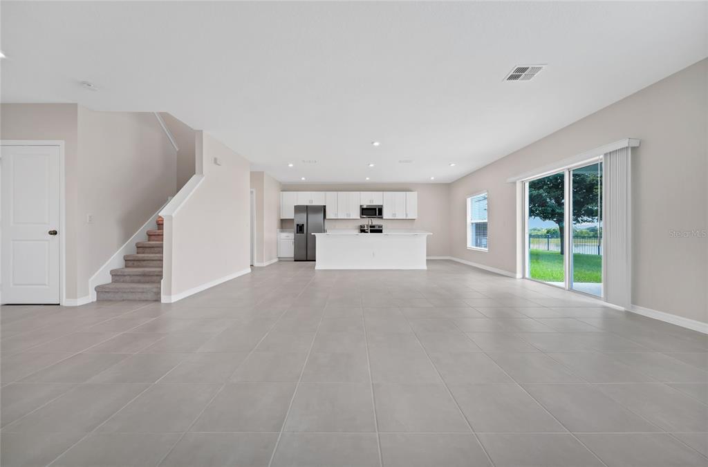 An open-concept living area features light gray tile flooring, a staircase, and a modern kitchen — 3800 FESCUE STREET, CLERMONT, FL