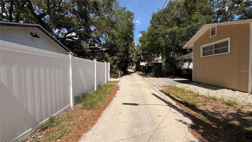A narrow paved alleyway runs between a white vinyl fence and a tan house — 905 JONES STREET, CLEARWATER, FL