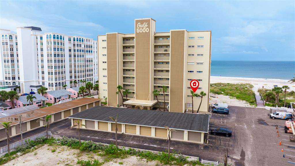 An aerial view shows a multi-story beachfront condominium building with an adjacent parking structure — 5000 GULF BOULEVARD UNIT 301, ST PETE BEACH, FL