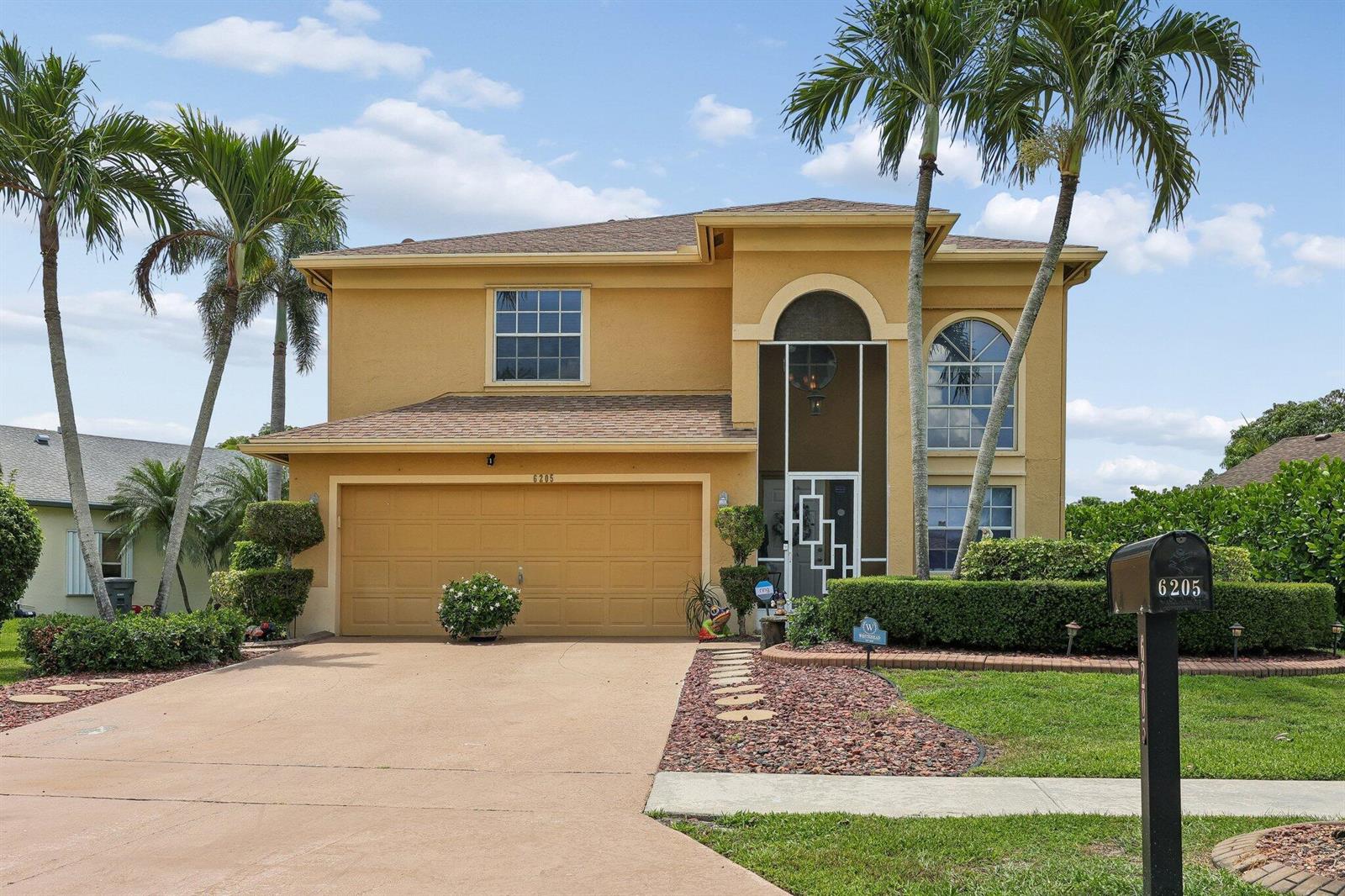 A two-story yellow stucco house features a two-car garage and a palm-lined front yard — 6205 Lansdowne Circle, Boynton Beach FL 33472, BOYNTON BEACH, FL