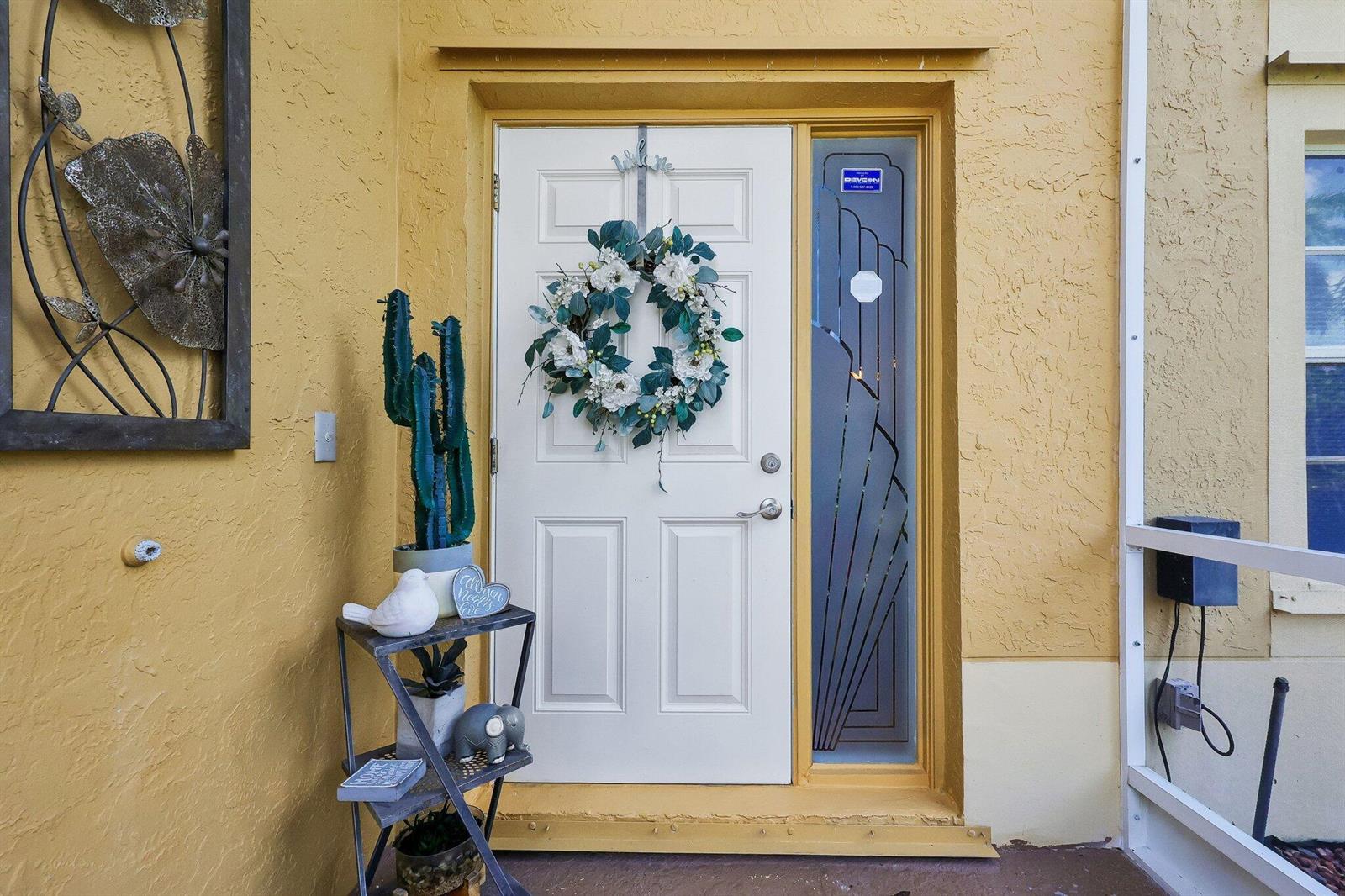 A white front door with a floral wreath sits beside a tall cactus on a stand — 6205 Lansdowne Circle, Boynton Beach FL 33472, BOYNTON BEACH, FL