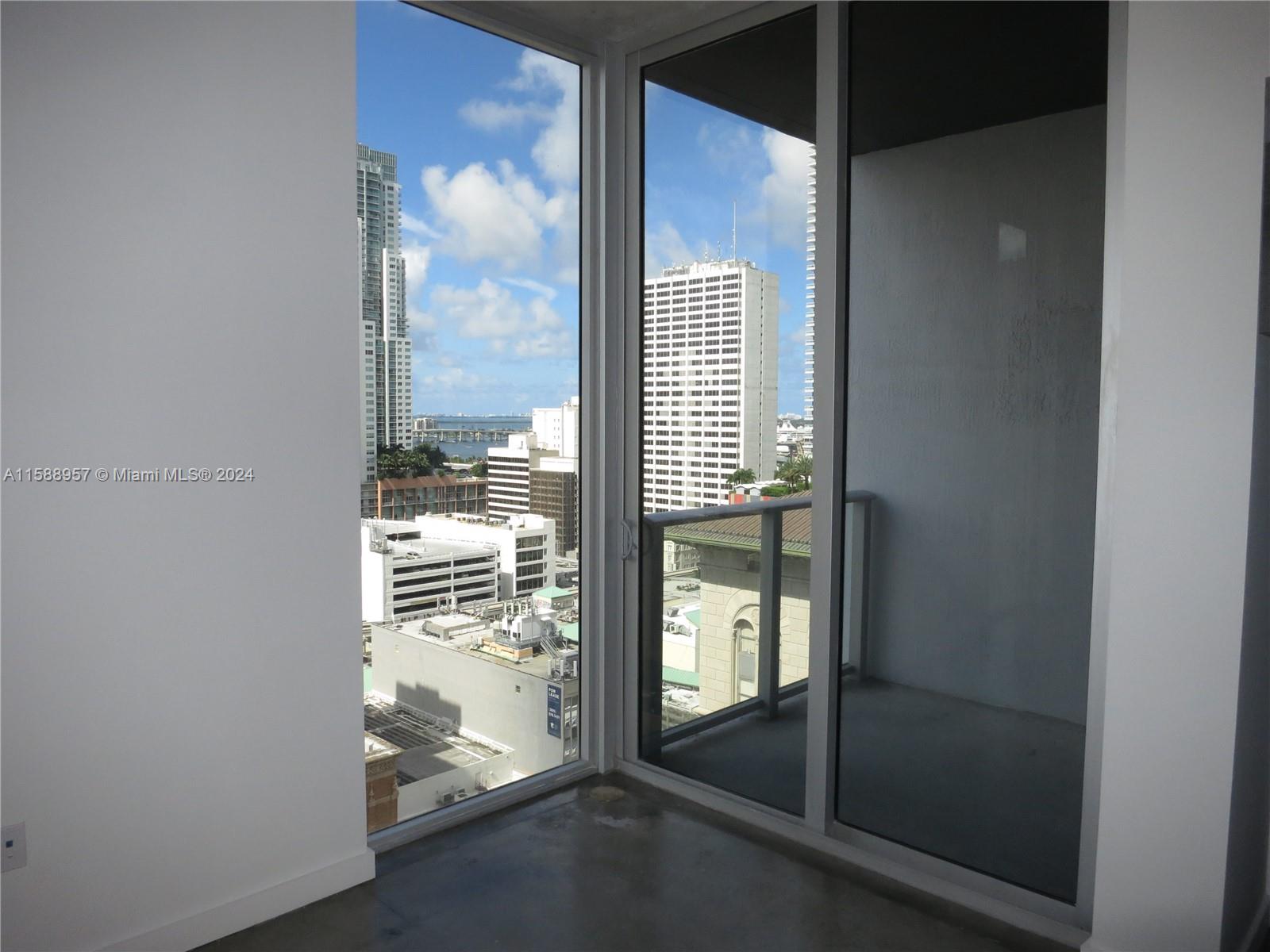 An interior room with concrete floors, floor-to-ceiling windows, and a balcony overlooking city buildings — 151 SE 1 St # 1704, Miami FL 33131, MIAMI, FL