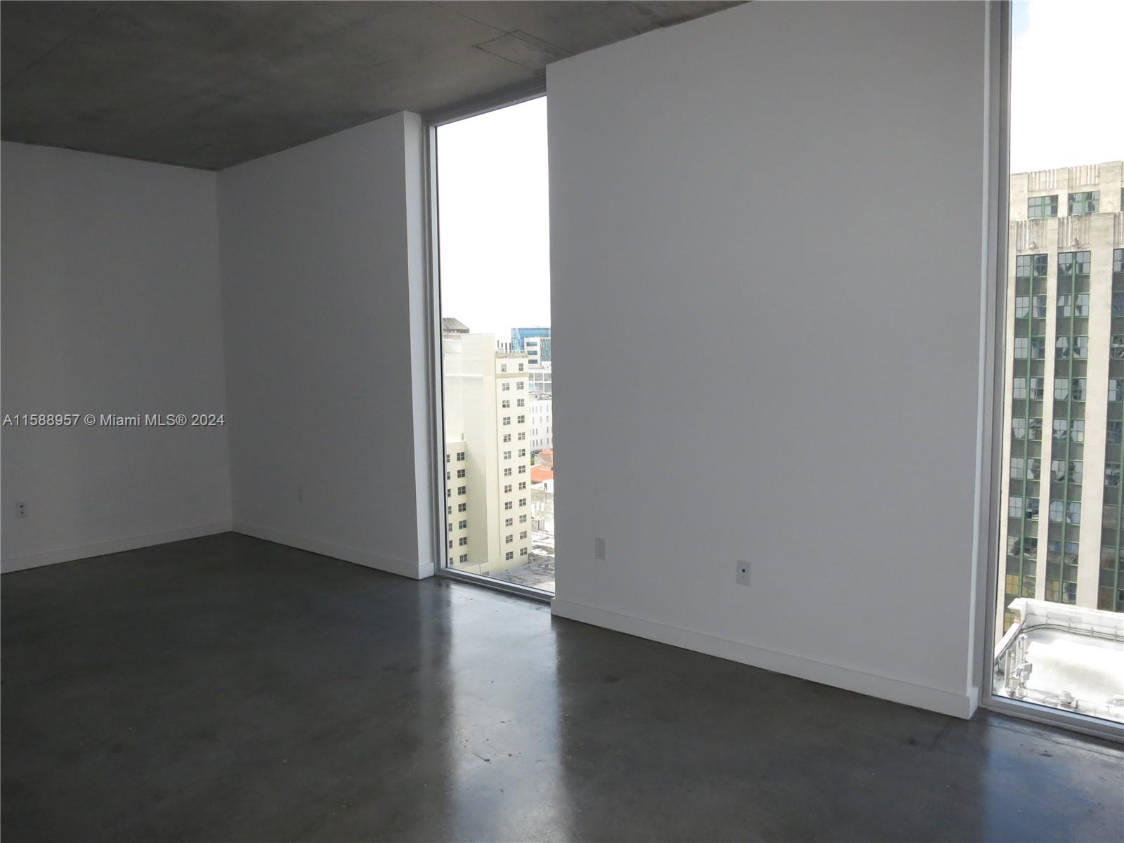 An empty room features polished concrete floors, white walls, and floor-to-ceiling windows overlooking city buildings — 151 SE 1 St # 1704, Miami FL 33131, MIAMI, FL