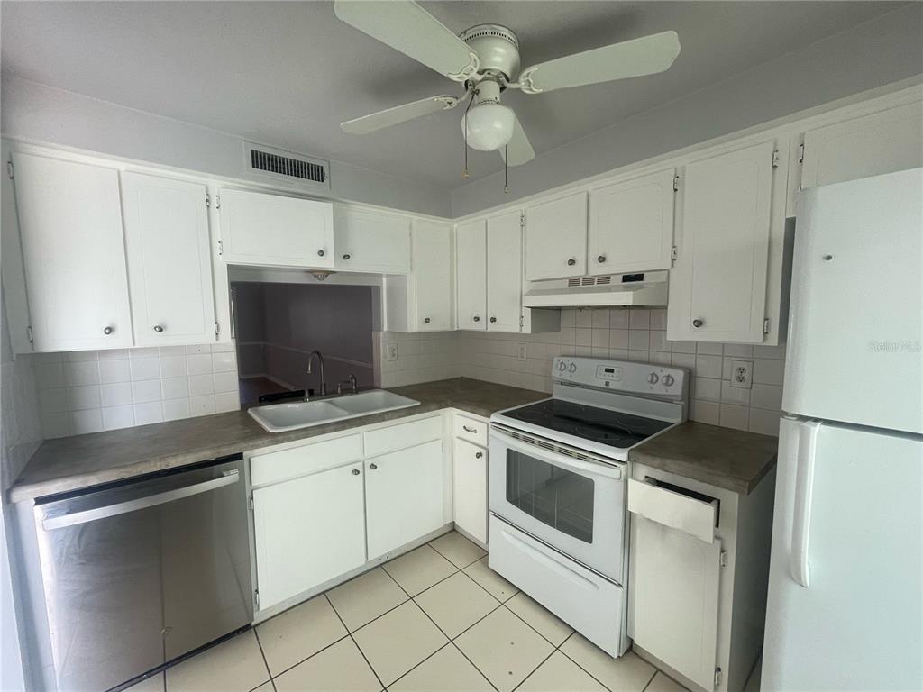 A kitchen features white cabinets, a stainless steel dishwasher, a white stove, and tiled floors — 4211 SHELDON PLACE UNIT 4211, NEW PORT RICHEY, FL