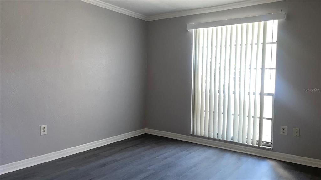 An empty room features gray walls, dark wood-look flooring, white baseboards, and vertical window blinds — 4211 SHELDON PLACE UNIT 4211, NEW PORT RICHEY, FL