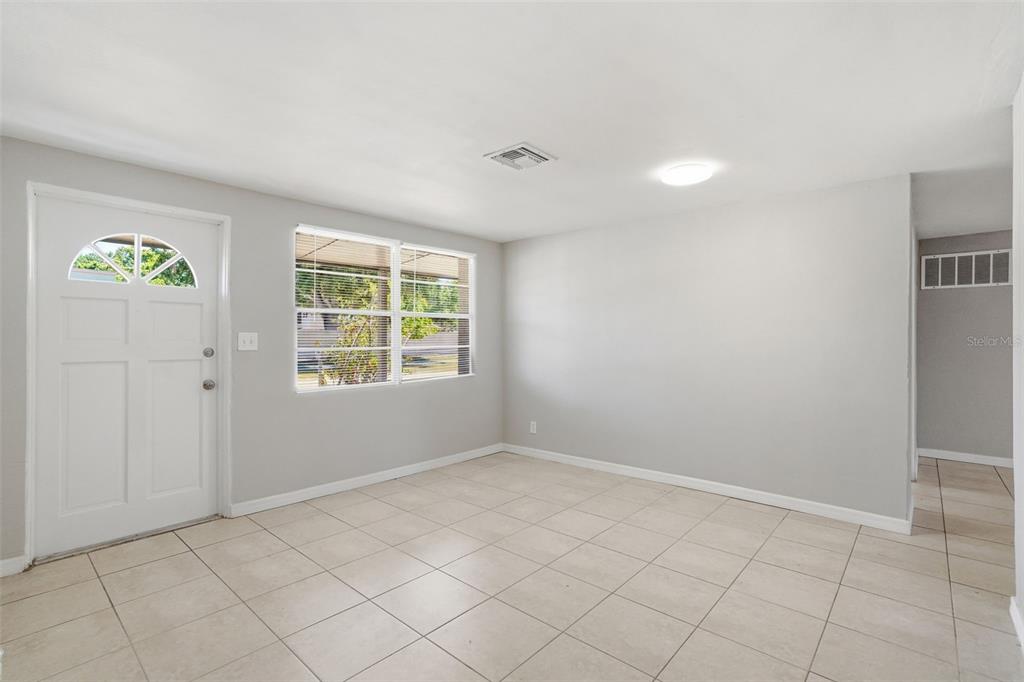 An empty room with light gray walls, tile flooring, a front door, and a window — 5711 64TH AVENUE N, PINELLAS PARK, FL