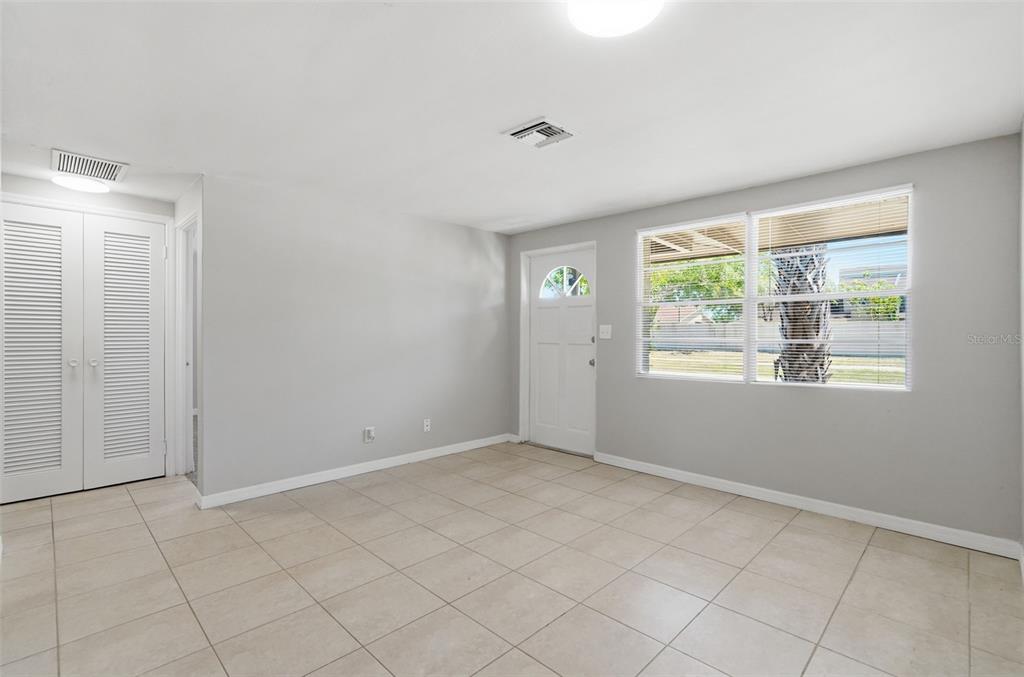 An empty room with light gray walls, beige tile flooring, a white door, and windows — 5711 64TH AVENUE N, PINELLAS PARK, FL