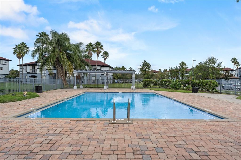 An outdoor rectangular swimming pool is surrounded by a brick paver deck and metal fencing — 5501 PGA BOULEVARD UNIT 4724, ORLANDO, FL