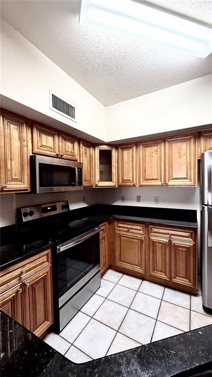 A kitchen features wood cabinets, black countertops, stainless steel appliances, and white tiled flooring — 832 CAMARGO WAY UNIT 307, ALTAMONTE SPRINGS, FL