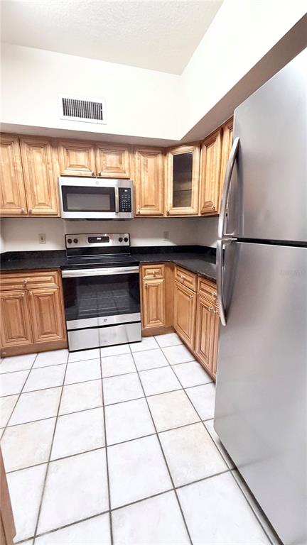 A kitchen features light wood cabinets, stainless steel appliances, dark countertops, and white tile flooring — 832 CAMARGO WAY UNIT 307, ALTAMONTE SPRINGS, FL