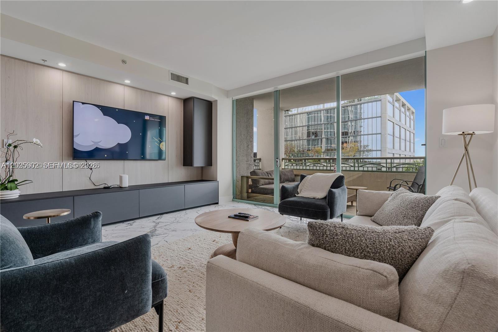 A modern living room features a wall-mounted television, dark cabinetry, and a balcony view — 3400 SW 27th Ave # 605, Miami FL 33133, MIAMI, FL