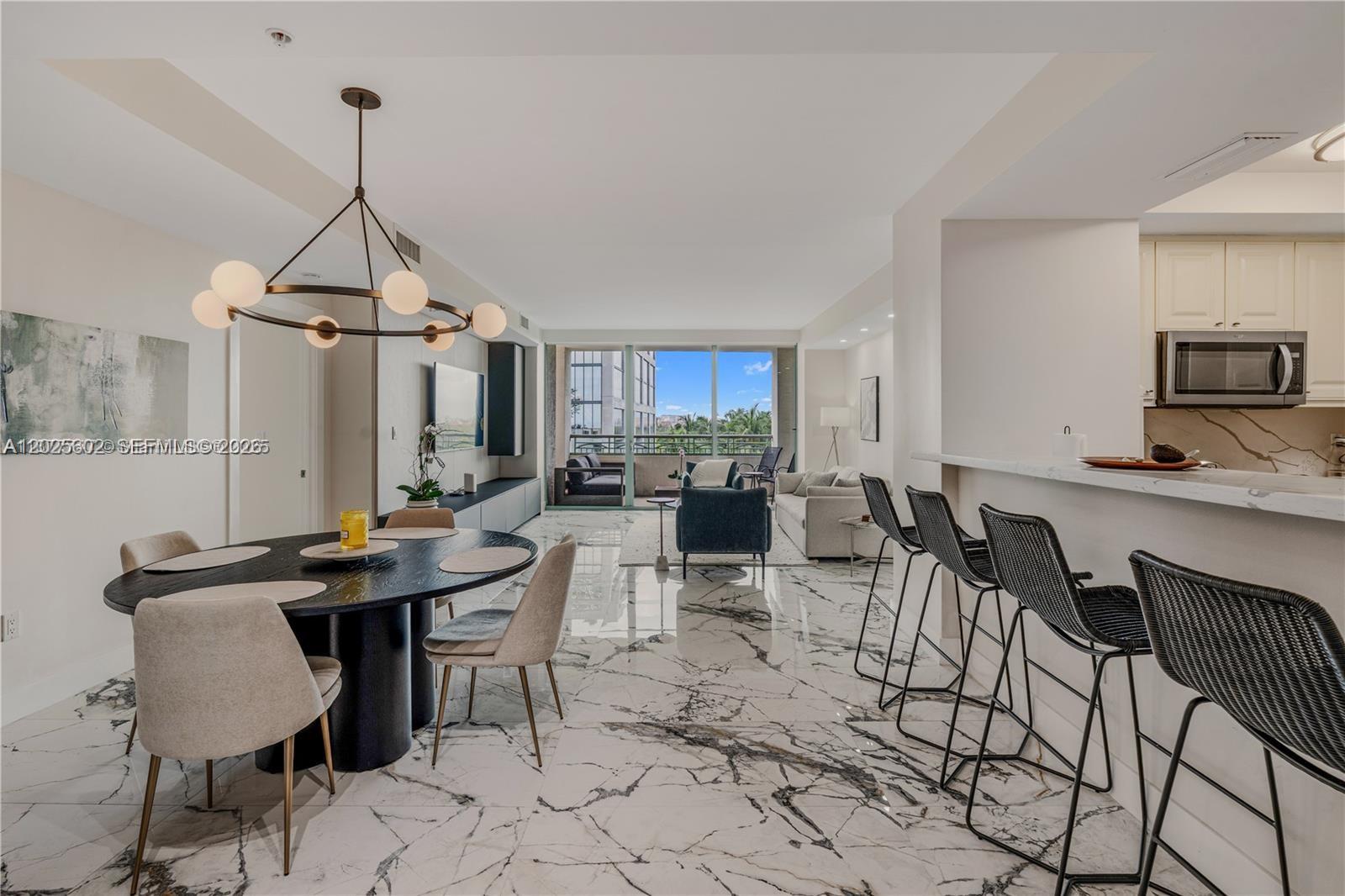 An open-concept living and dining area features marble flooring, a modern chandelier, and kitchen bar seating — 3400 SW 27th Ave # 605, Miami FL 33133, MIAMI, FL