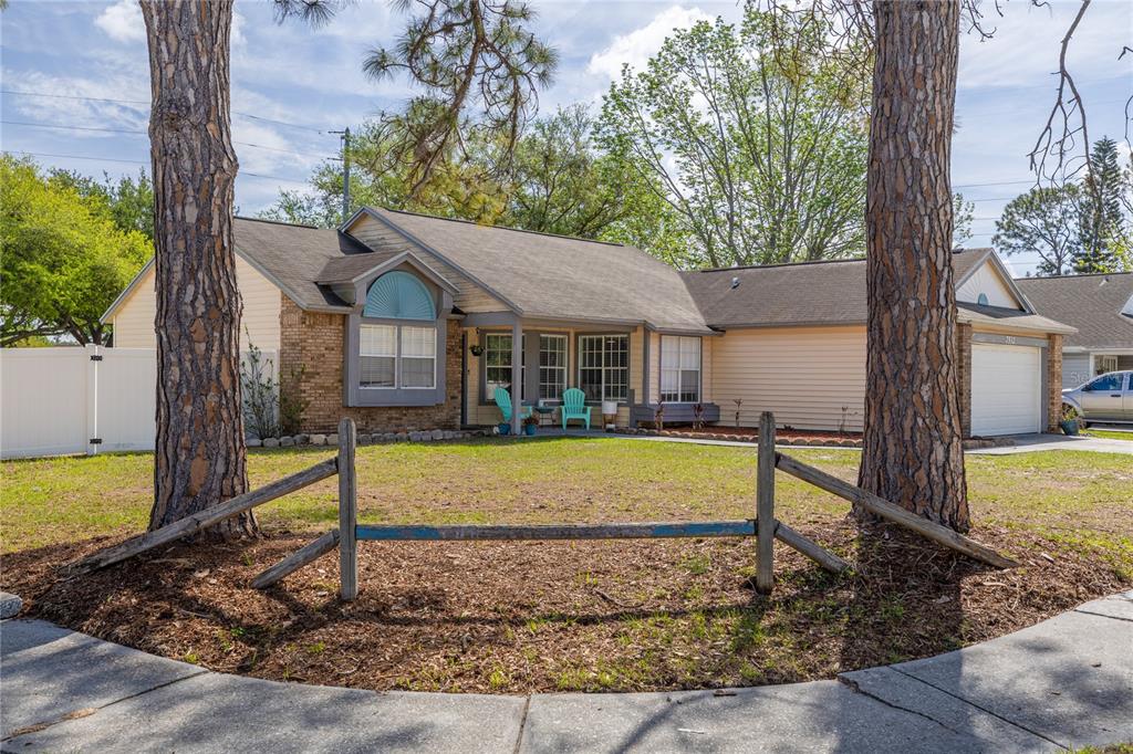 A single-story house with light siding and brick accents sits behind a wooden fence — 7532 TURTLEBROOK LANE, NEW PORT RICHEY, FL