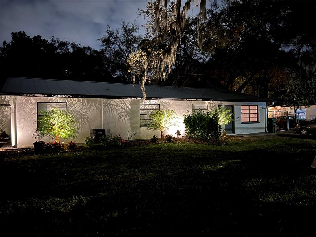 A single-story house exterior at night with illuminated landscaping and palm trees against the wall — 302 19TH ST. EAST, BRADENTON, FL
