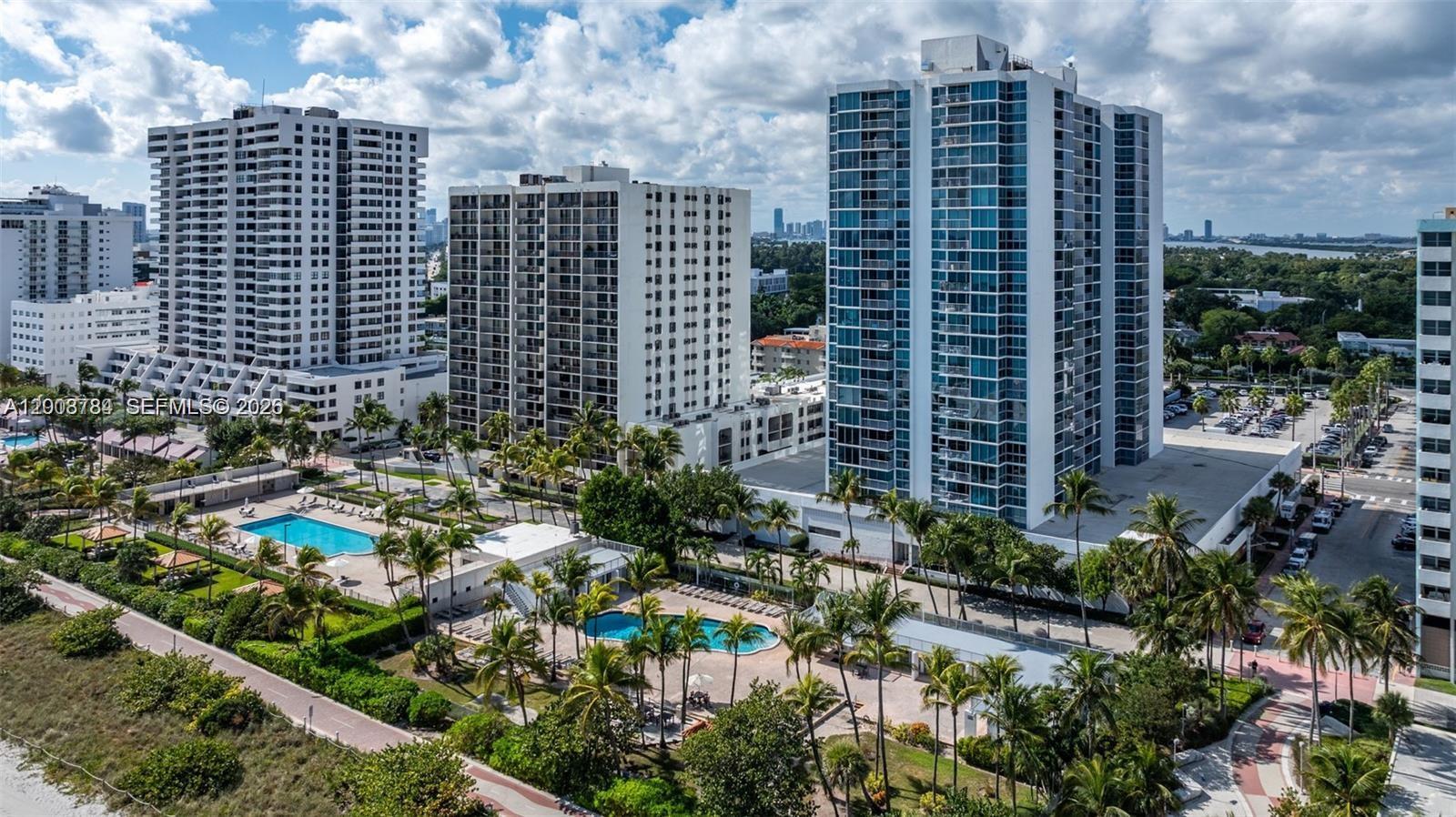 An aerial view shows multiple high-rise apartment buildings with swimming pools and palm trees below — 2655 Collins Ave # 2406, Miami Beach FL 33140, MIAMI BEACH, FL