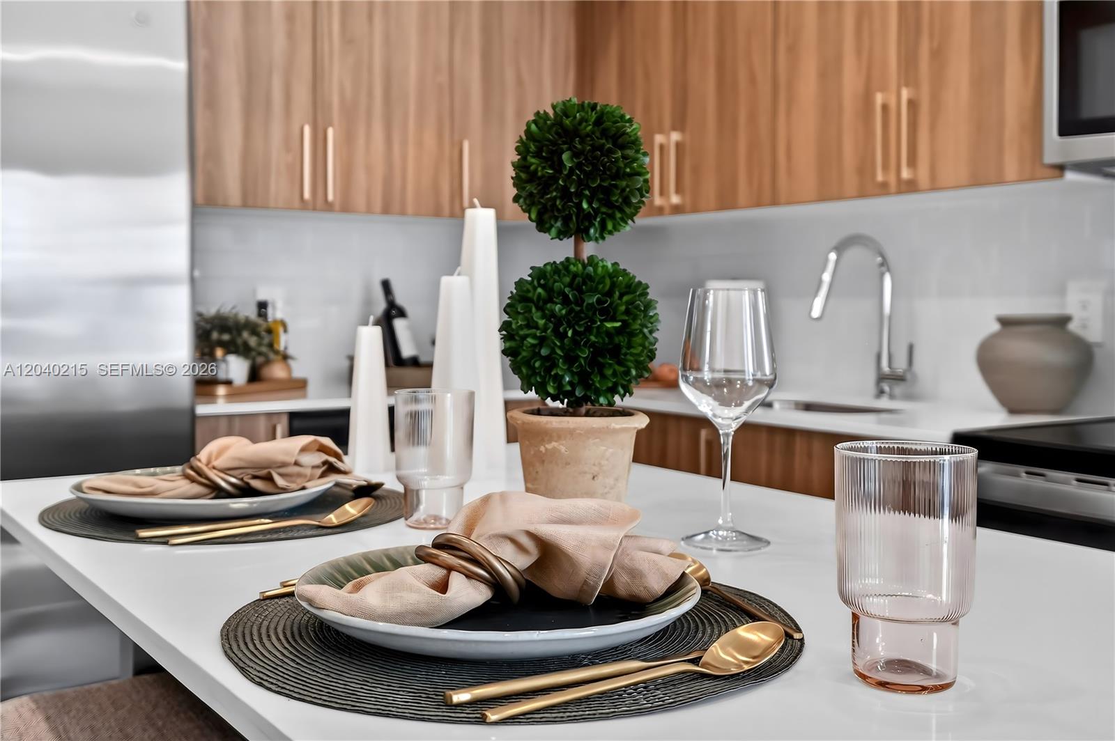 A kitchen island is set for dining with plates, napkins, glassware, and gold-toned cutlery — 2001 Van Buren St # 504, Hollywood FL 33020, HOLLYWOOD, FL