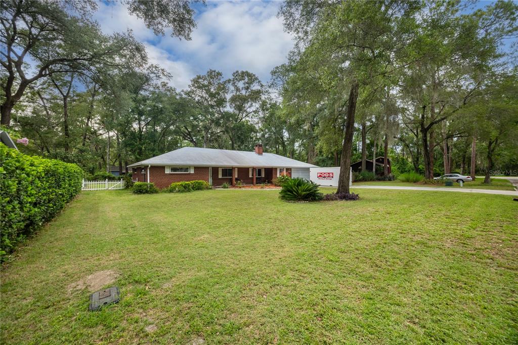 A single-story brick house with a white roof sits on a large, tree-lined grassy lot — 130 SW 75TH TERRACE, GAINESVILLE, FL