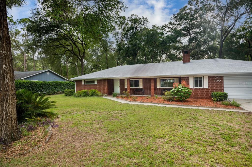 A single-story brick house with a white roof and a front lawn with trees — 130 SW 75TH TERRACE, GAINESVILLE, FL