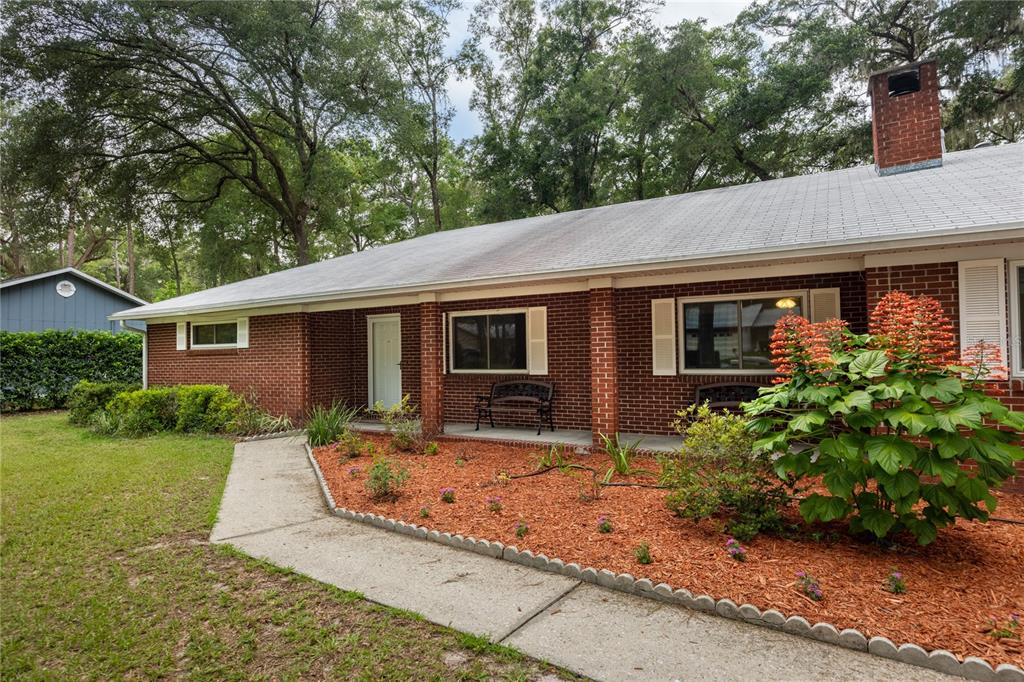 A brick ranch-style house features a covered porch, a concrete walkway, and a landscaped yard — 130 SW 75TH TERRACE, GAINESVILLE, FL