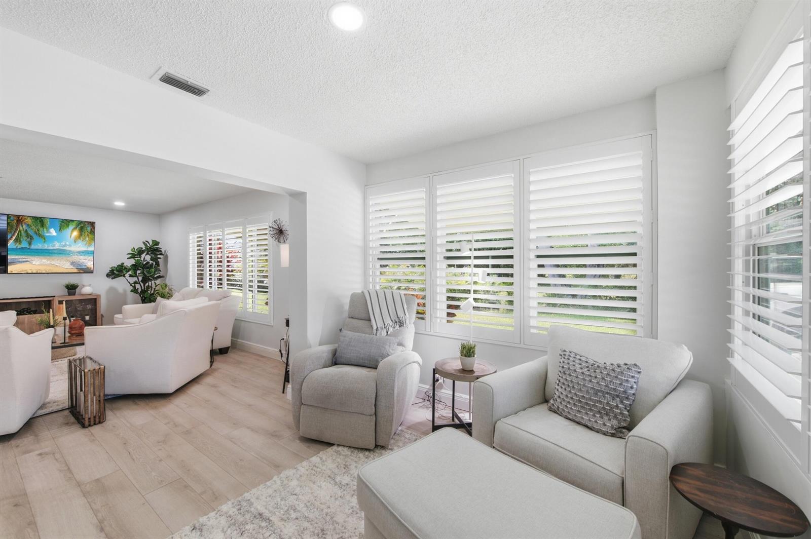 A bright living room features white plantation shutters, light wood flooring, and neutral-toned furniture — 957 Circle Drive # D, Delray Beach FL 33445, DELRAY BEACH, FL