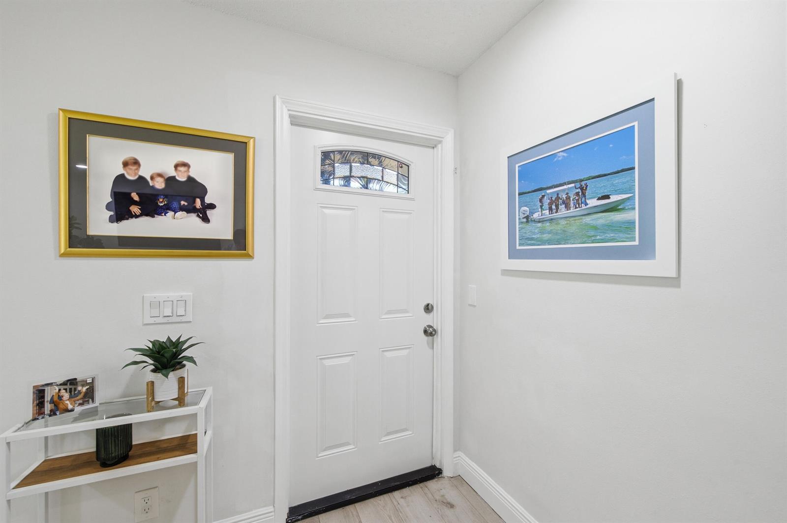 An entryway features a white door, light wood flooring, and framed wall art — 957 Circle Drive # D, Delray Beach FL 33445, DELRAY BEACH, FL