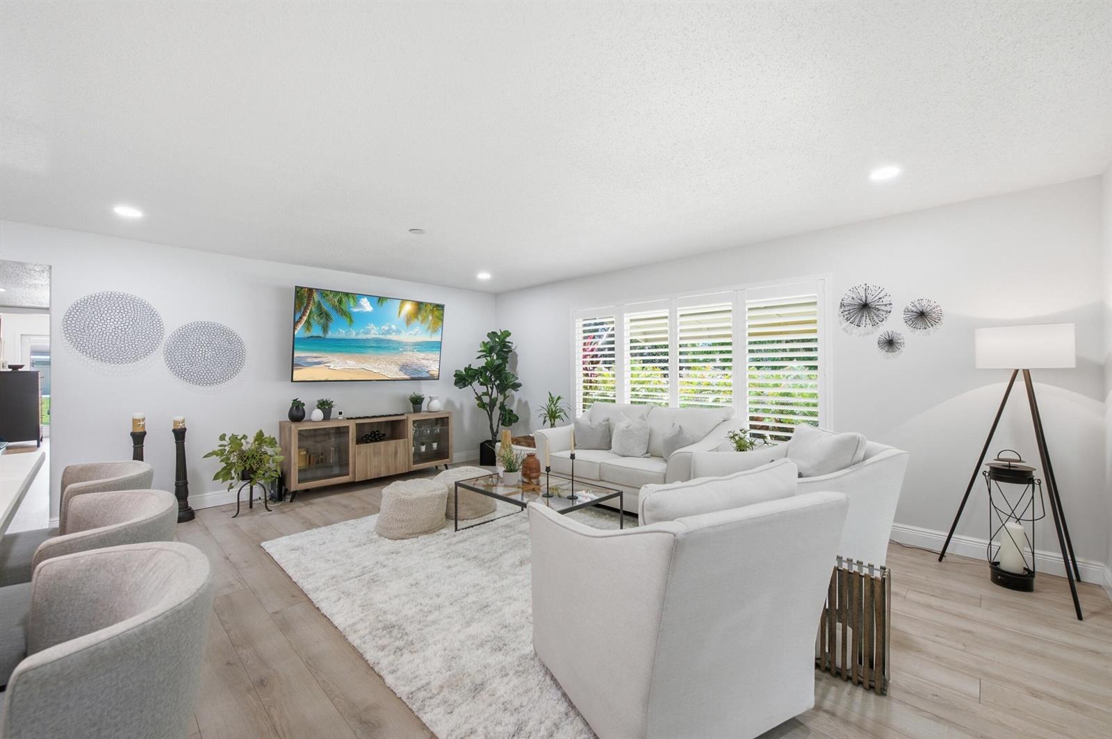 A bright living room features white furniture, a large area rug, and a wall-mounted television — 957 Circle Drive # D, Delray Beach FL 33445, DELRAY BEACH, FL